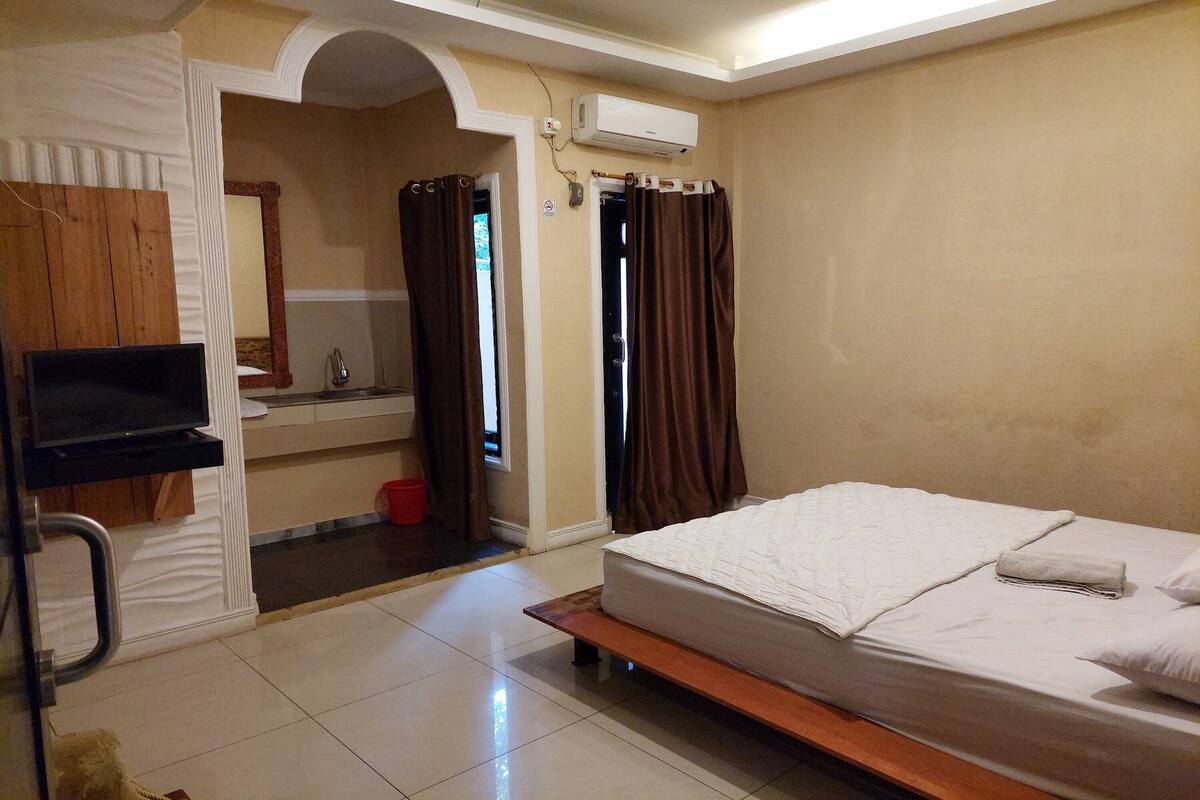 A hotel room with a bed, a TV, a bathroom, and a window with curtains.