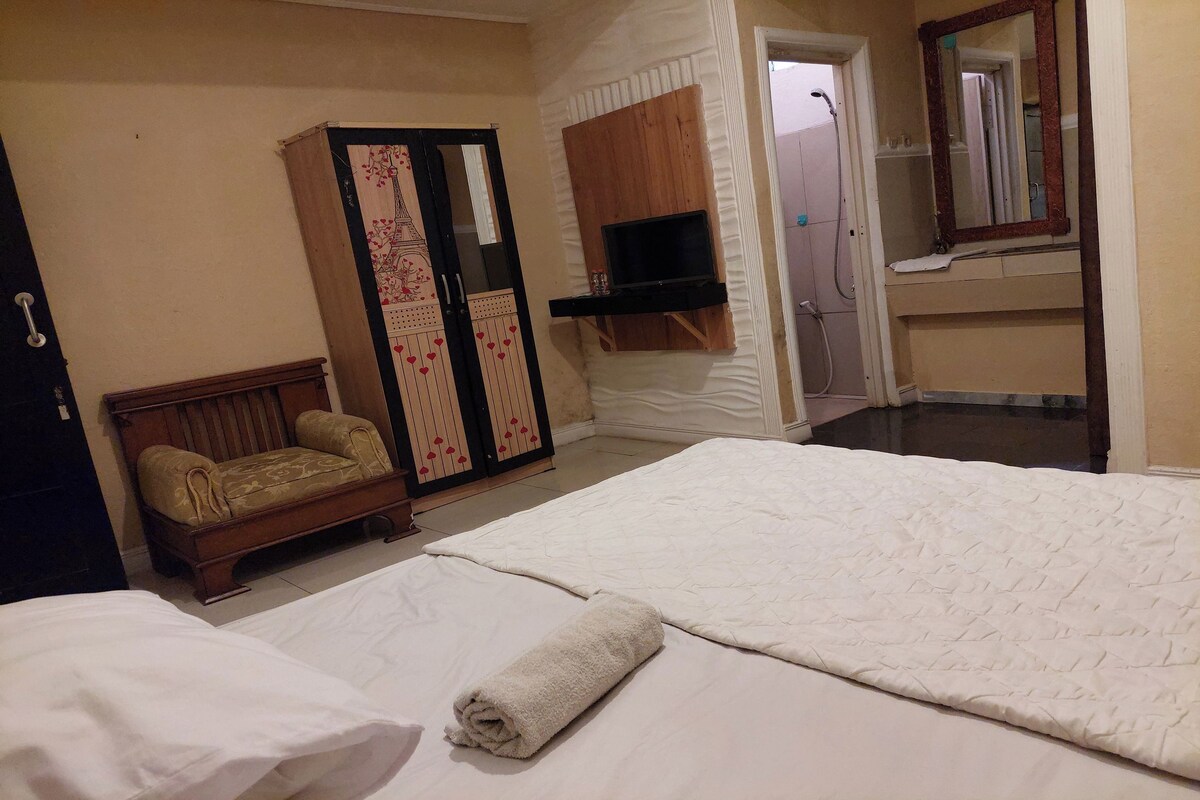 A hotel room with a bed, a wooden wardrobe, a television, and a bathroom with a mirror.