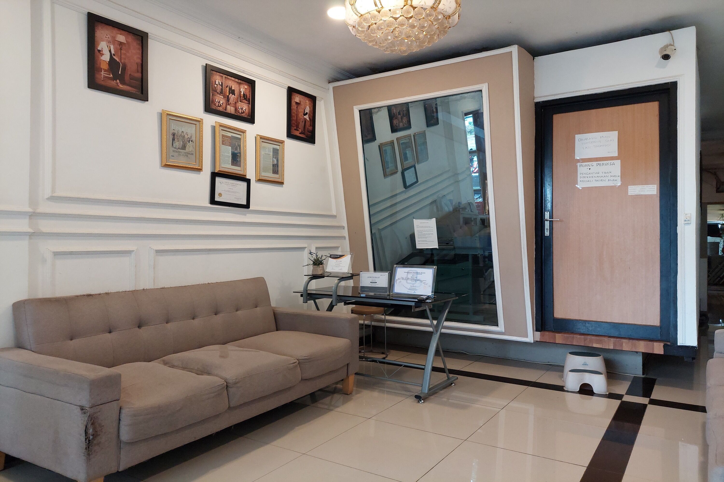 Un área de recepción con un sofá beige, cuadros enmarcados en la pared, una vitrina de cristal y una puerta de madera con un letrero.