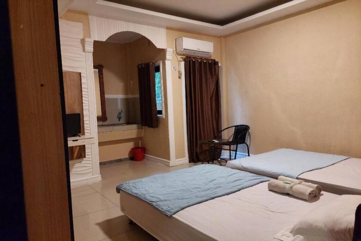 A hotel room with two beds, a desk with a chair, an air conditioning unit, and a window with curtains.