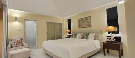 A spacious bedroom with a large bed, a small sofa, a nightstand, and a door leading to another room.