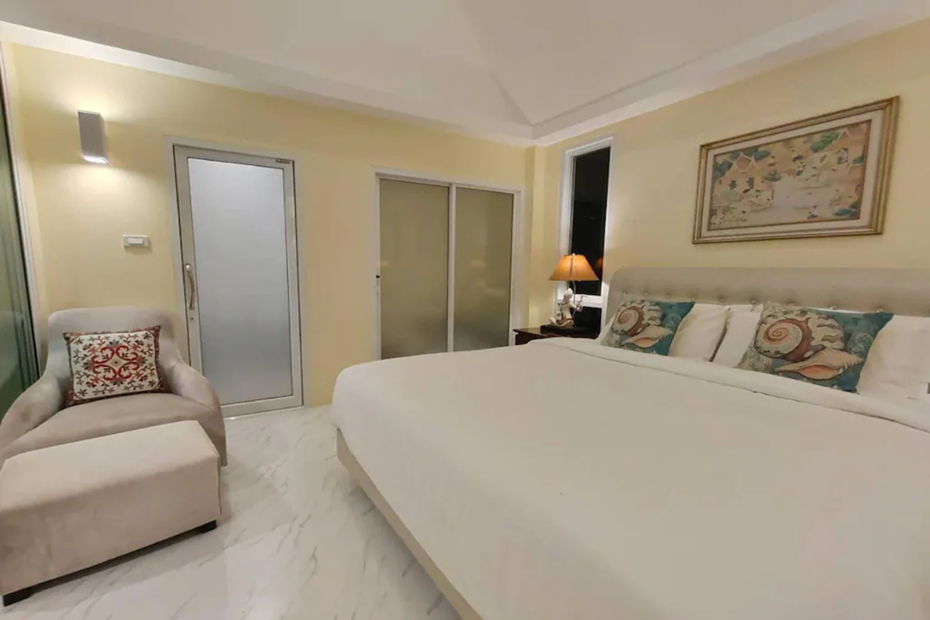 A hotel room with a large bed, a chair, a wardrobe, and a painting on the wall.