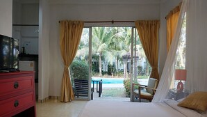 A hotel room with a bed, a TV, a desk, and a view of a pool and palm trees. - Kalamona Seaview (Sam Roi Yot)