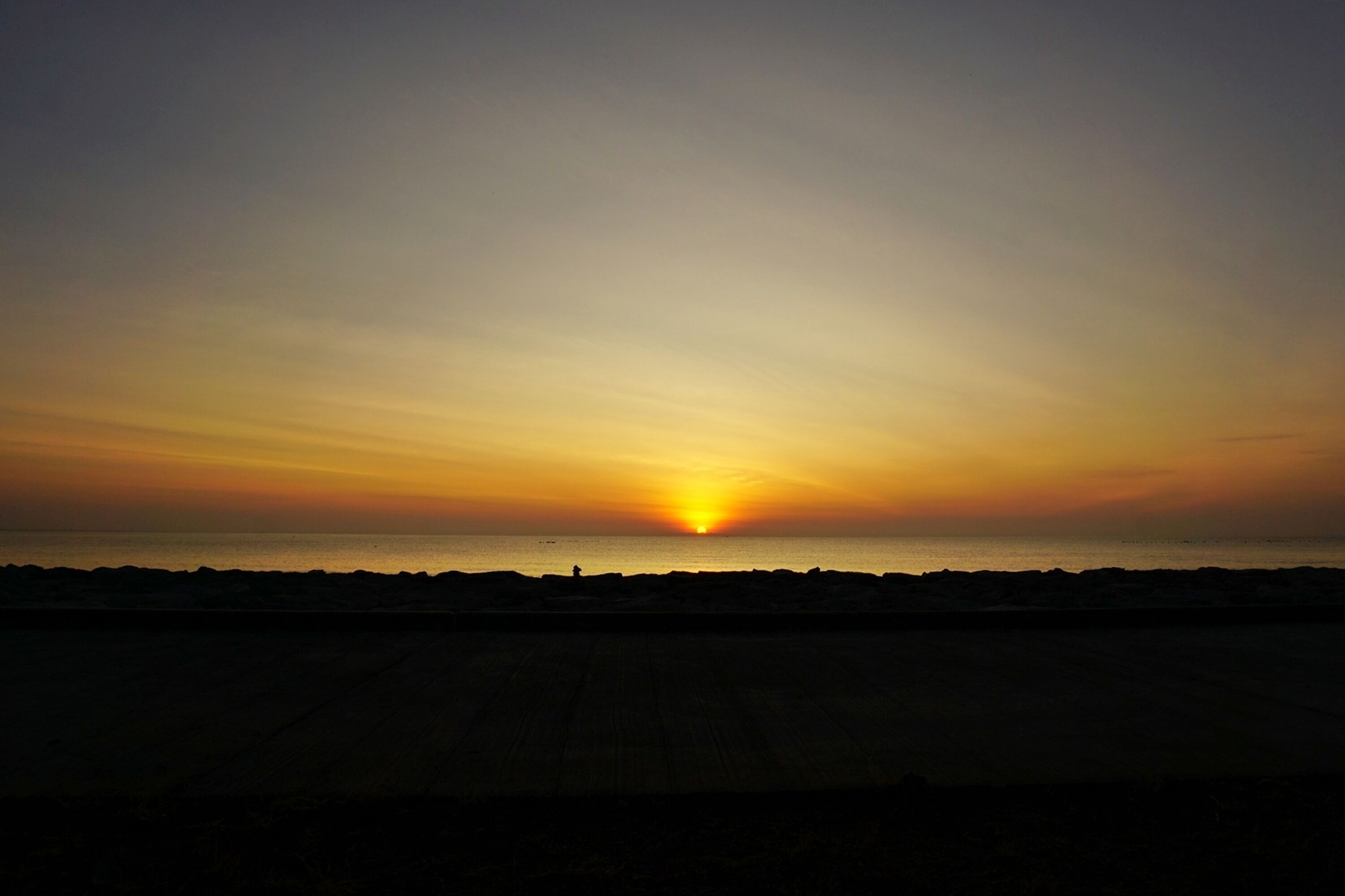 A sunset over a beach with a silhouette of a person in the distance.