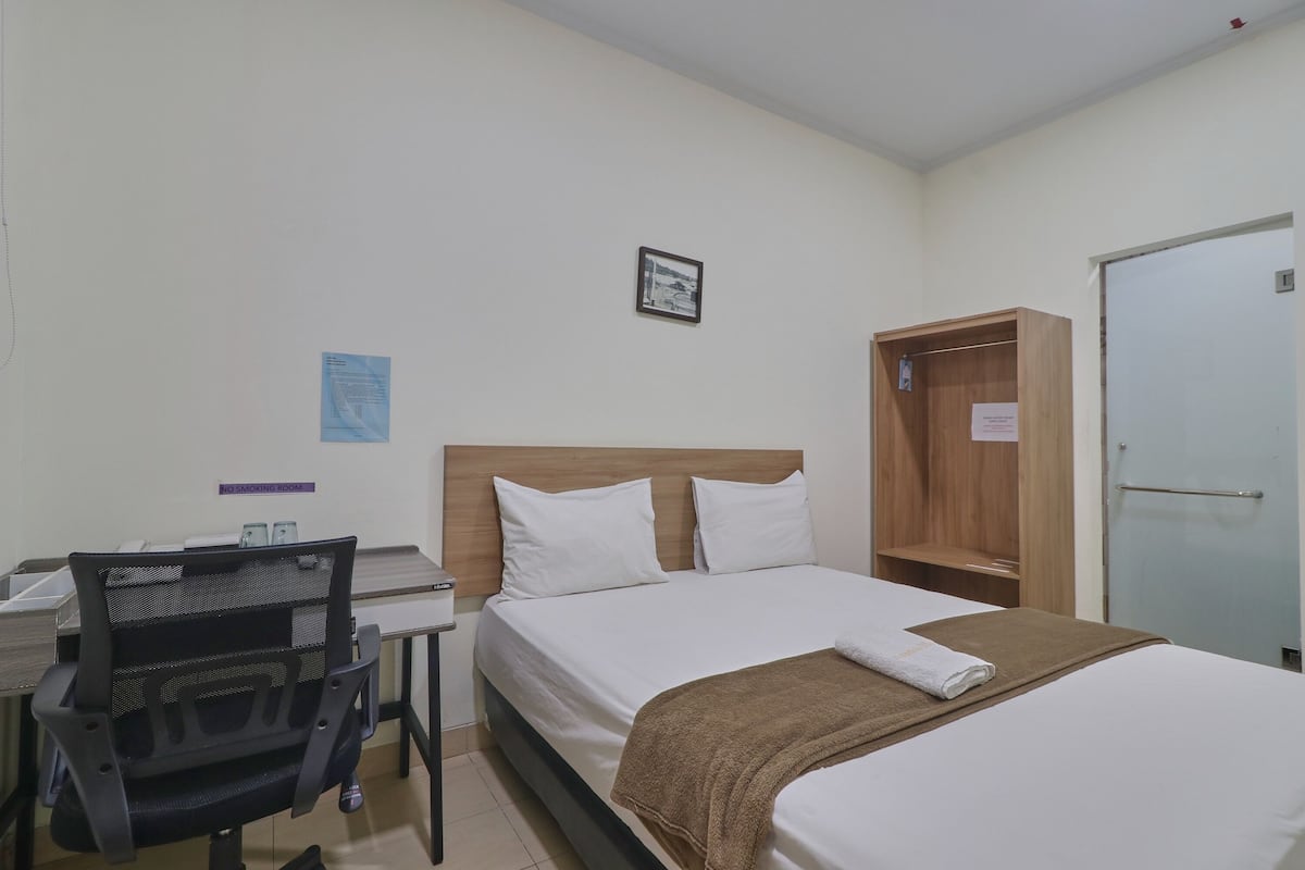A hotel room with a bed, a desk with a chair, a wardrobe, and a door.