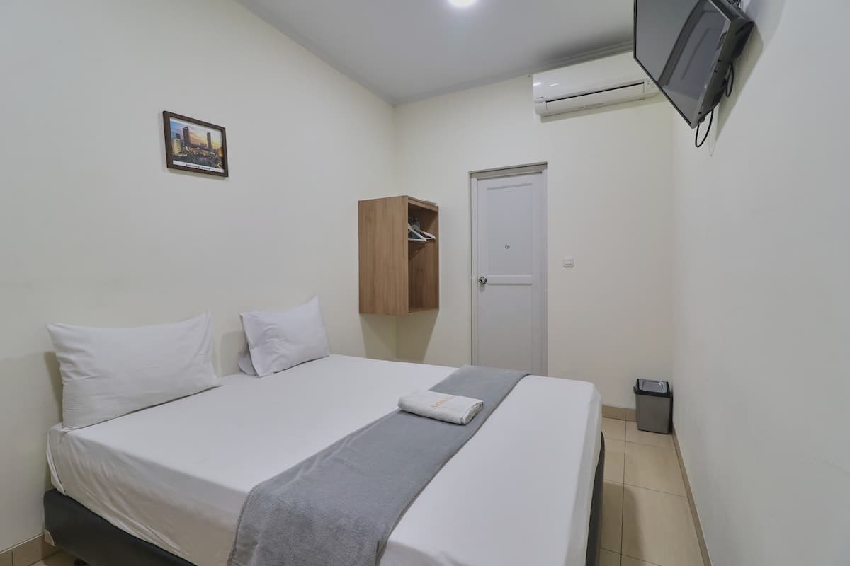 A neatly made bed with white linens and a gray throw blanket, a wooden wardrobe, a white door, and a mounted television on the wall.