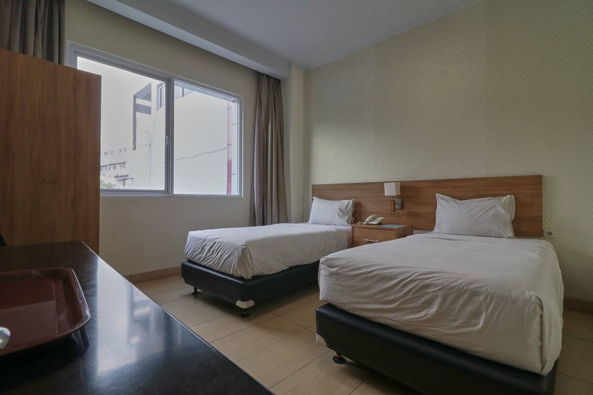 A hotel room with two beds, a desk, and a window with curtains.