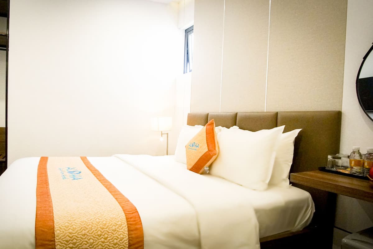 A hotel room with a bed, a wooden headboard, a nightstand with a lamp, and a wall-mounted mirror.
