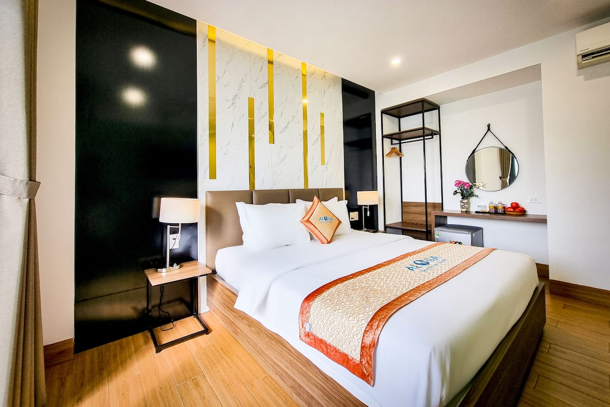 A modern hotel room with a large bed, bedside tables, a mirror, and a wall-mounted shelf with toiletries.