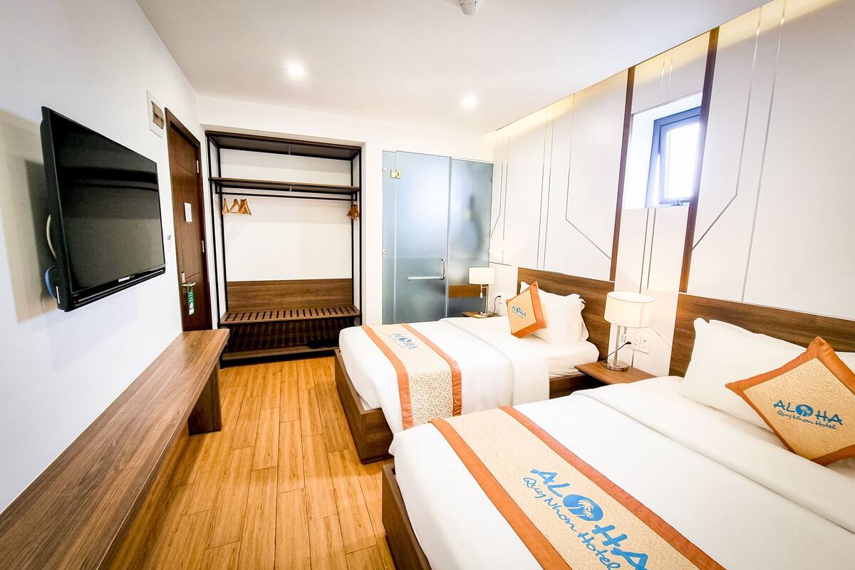 A hotel room with two beds, a bench, a TV, and a wardrobe.