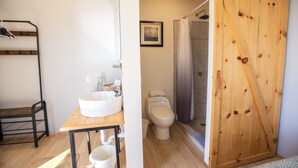 A bathroom with a sink, toilet, and shower. There is a wooden door and a rack with clothes. - Rosarito Beach Rooms #2 (Rosarito)