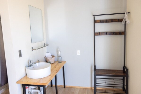 A bathroom with a wooden vanity, a white sink, a mirror, and a metal shelf.