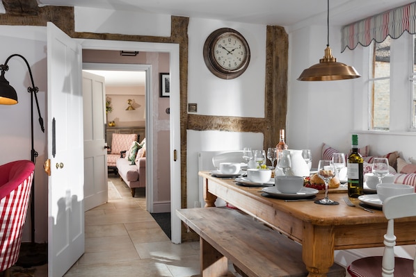 A dining area with a wooden table set for a meal, a clock on the wall, and a view into another room.