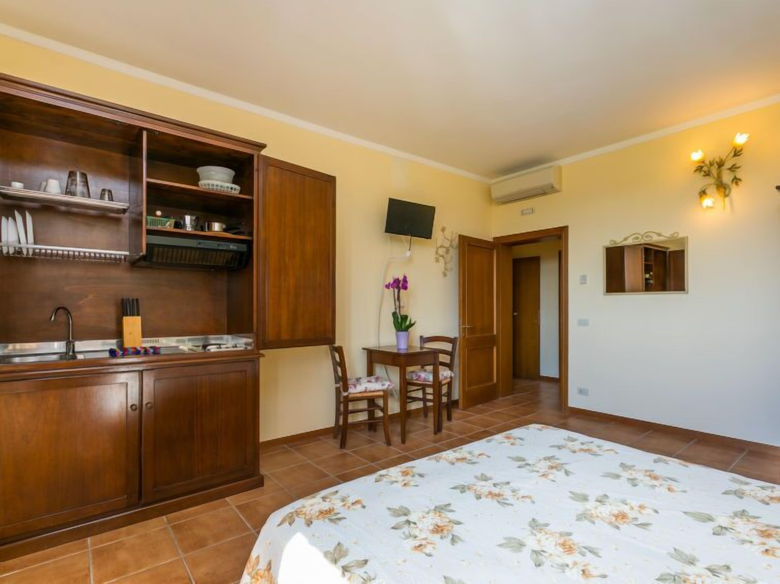 Een slaapkamer met een bed, een houten garderobe, een kleine tafel met stoelen, een aan de muur bevestigde televisie en een deur naar een andere kamer.