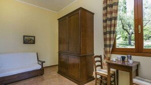 A room with a wooden wardrobe, a white sofa, a dining table with chairs, and a window with curtains. - Tipologia Bilo by Interhome (Vinci)