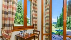 A dining area with a table and chairs, a window with curtains, and a view of a garden and trees. - Tipologia Bilo by Interhome (Vinci)