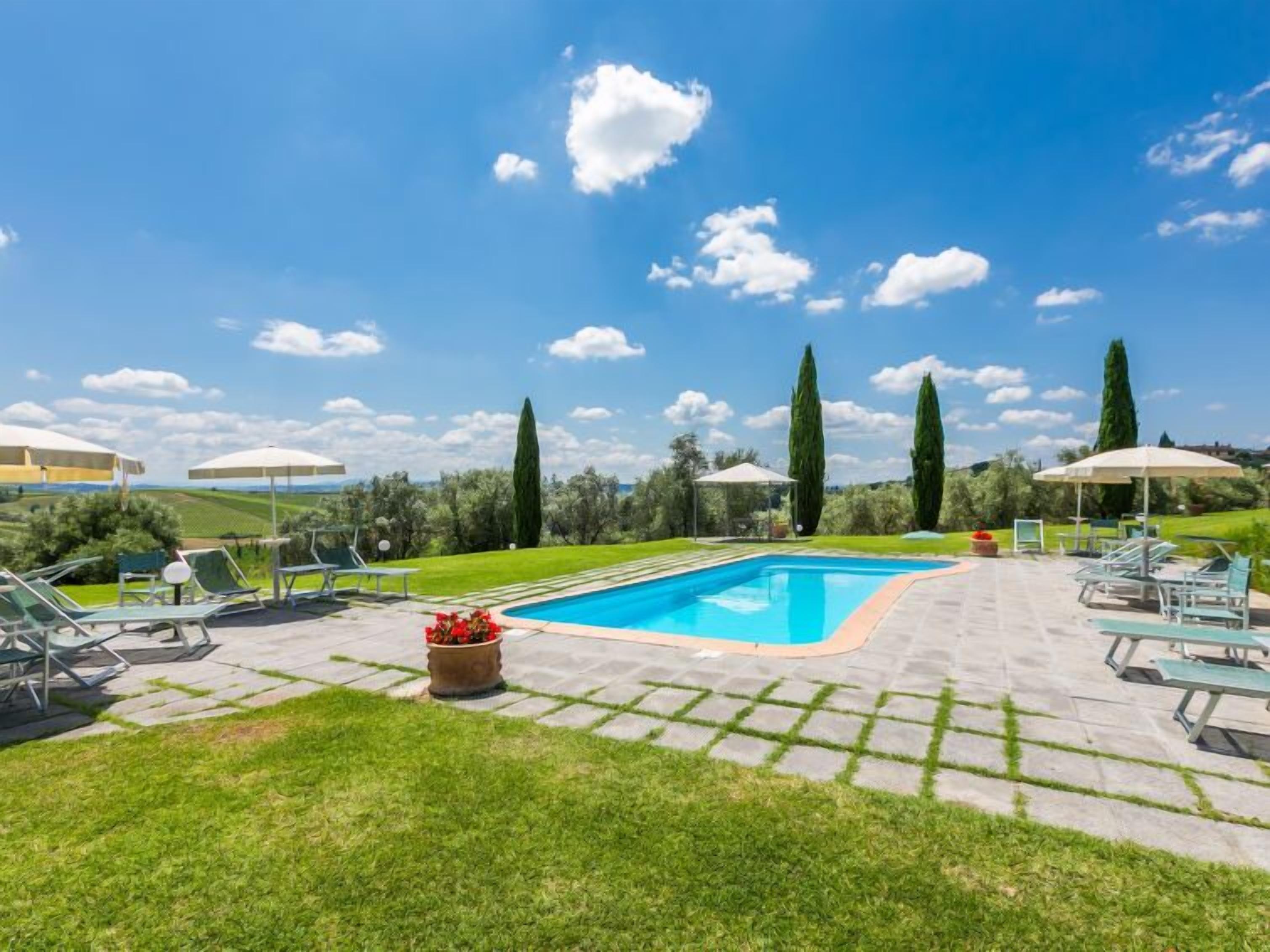 A swimming pool with lounge chairs and umbrellas, surrounded by well-maintained grass and trees.