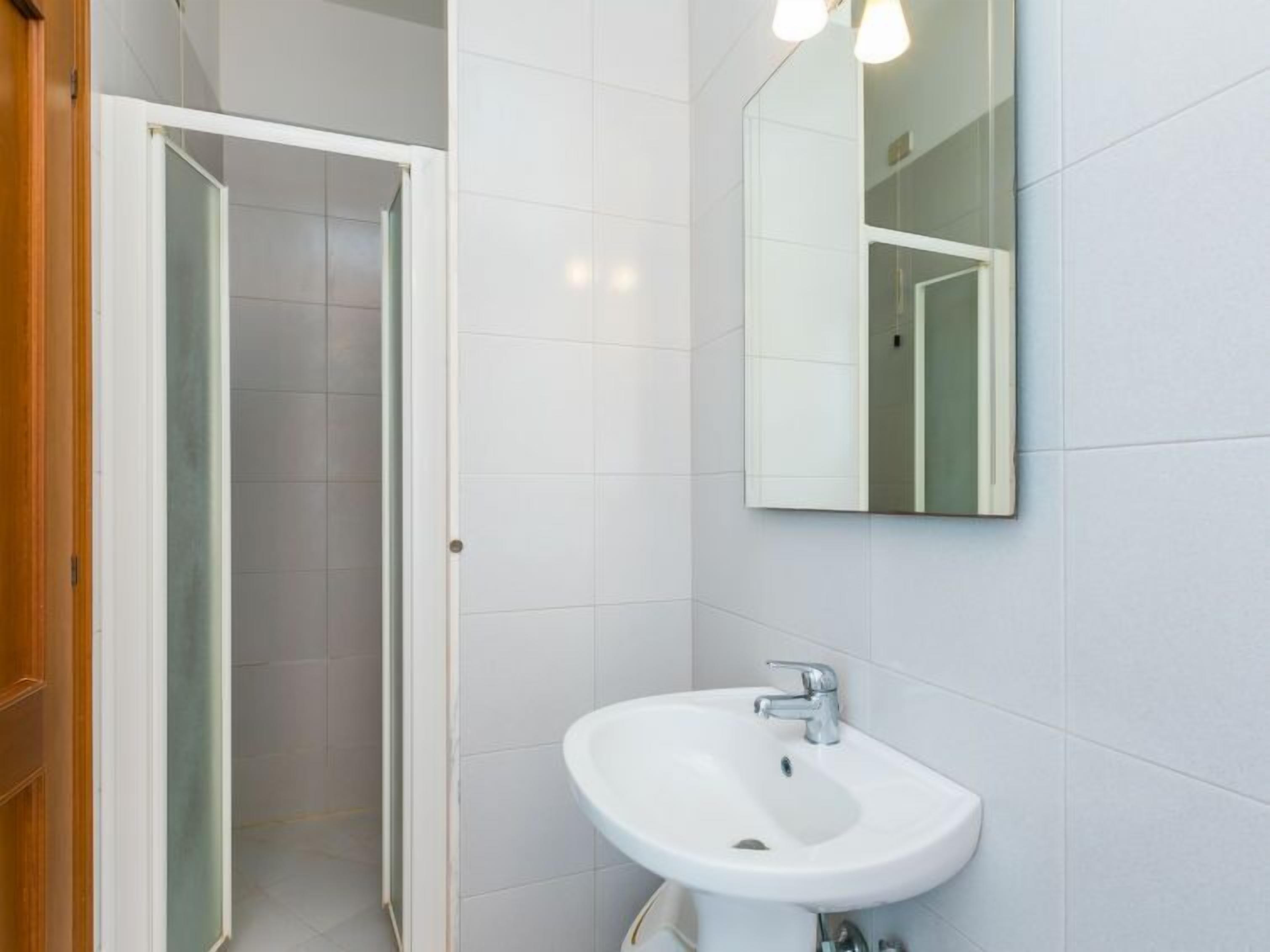 Une salle de bain moderne avec un lavabo blanc, un miroir et une porte donnant sur une autre pièce.