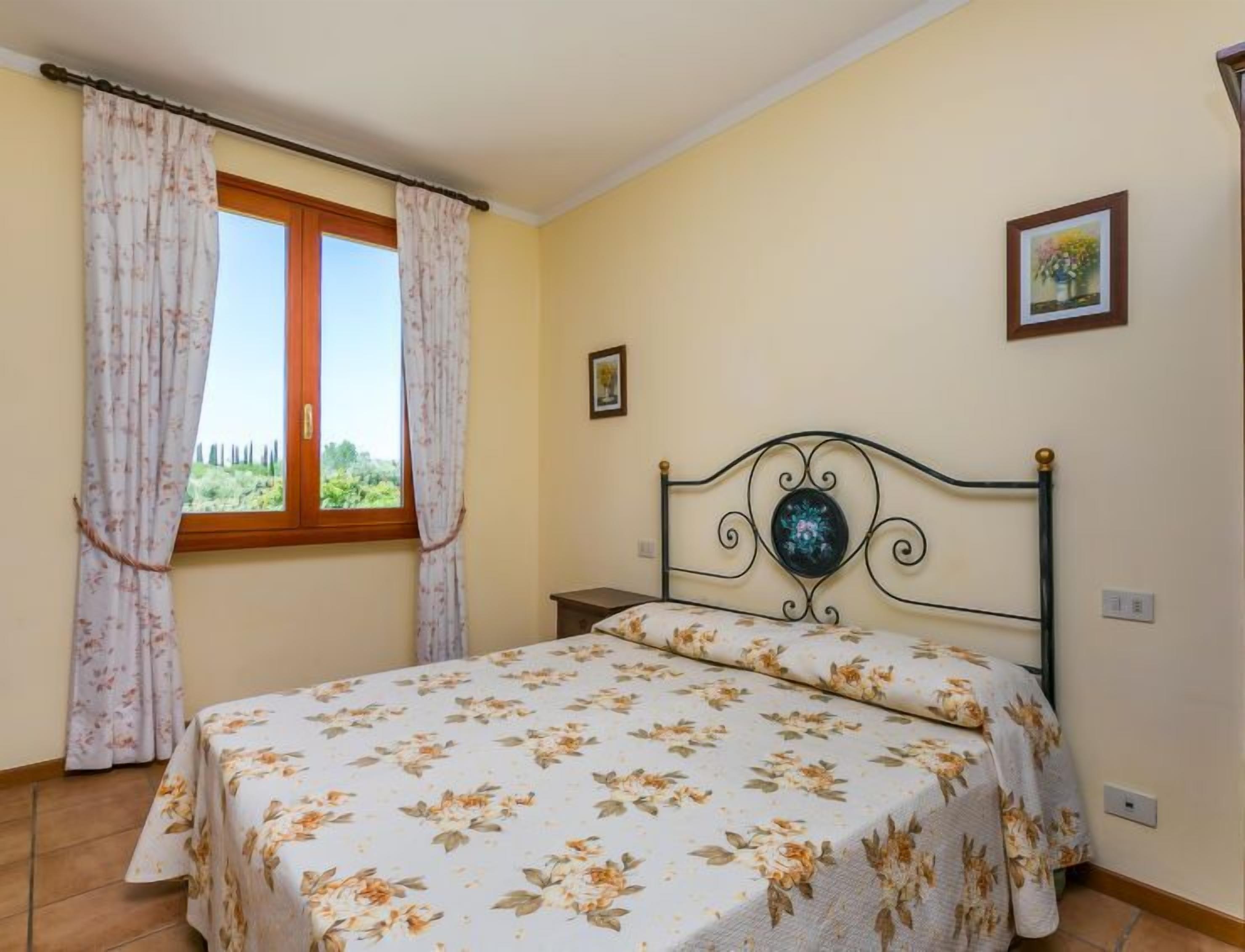 Une chambre à coucher avec un lit, une fenêtre avec des rideaux, une table de chevet et un tableau accroché au mur.