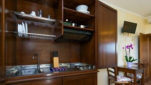A compact kitchen with wooden cabinets, a stainless steel sink, and a small dining area with a chair and table.