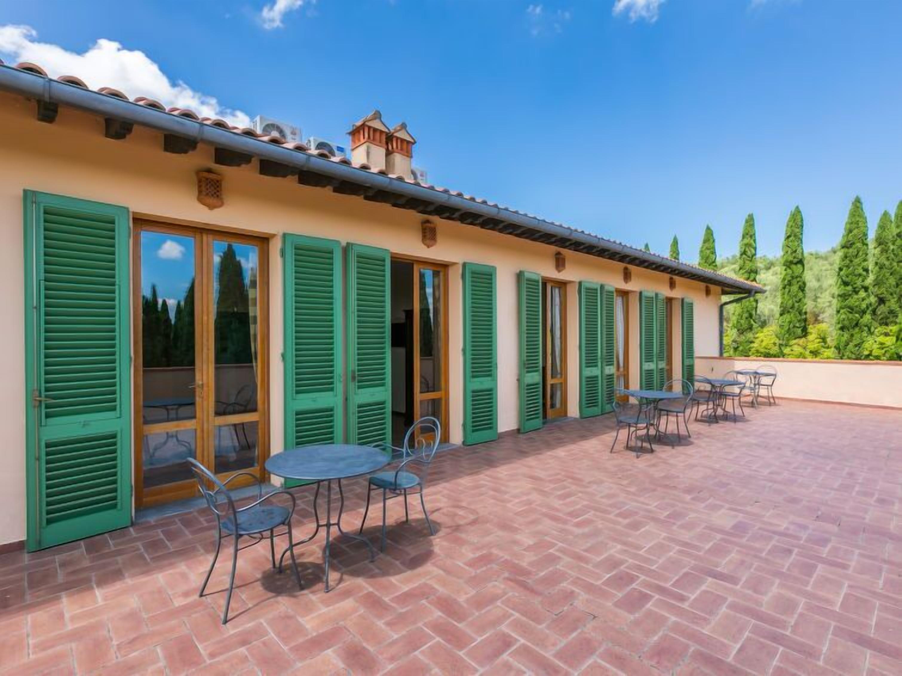Un edificio con techo de tejas, contraventanas verdes y un patio con mobiliario exterior.