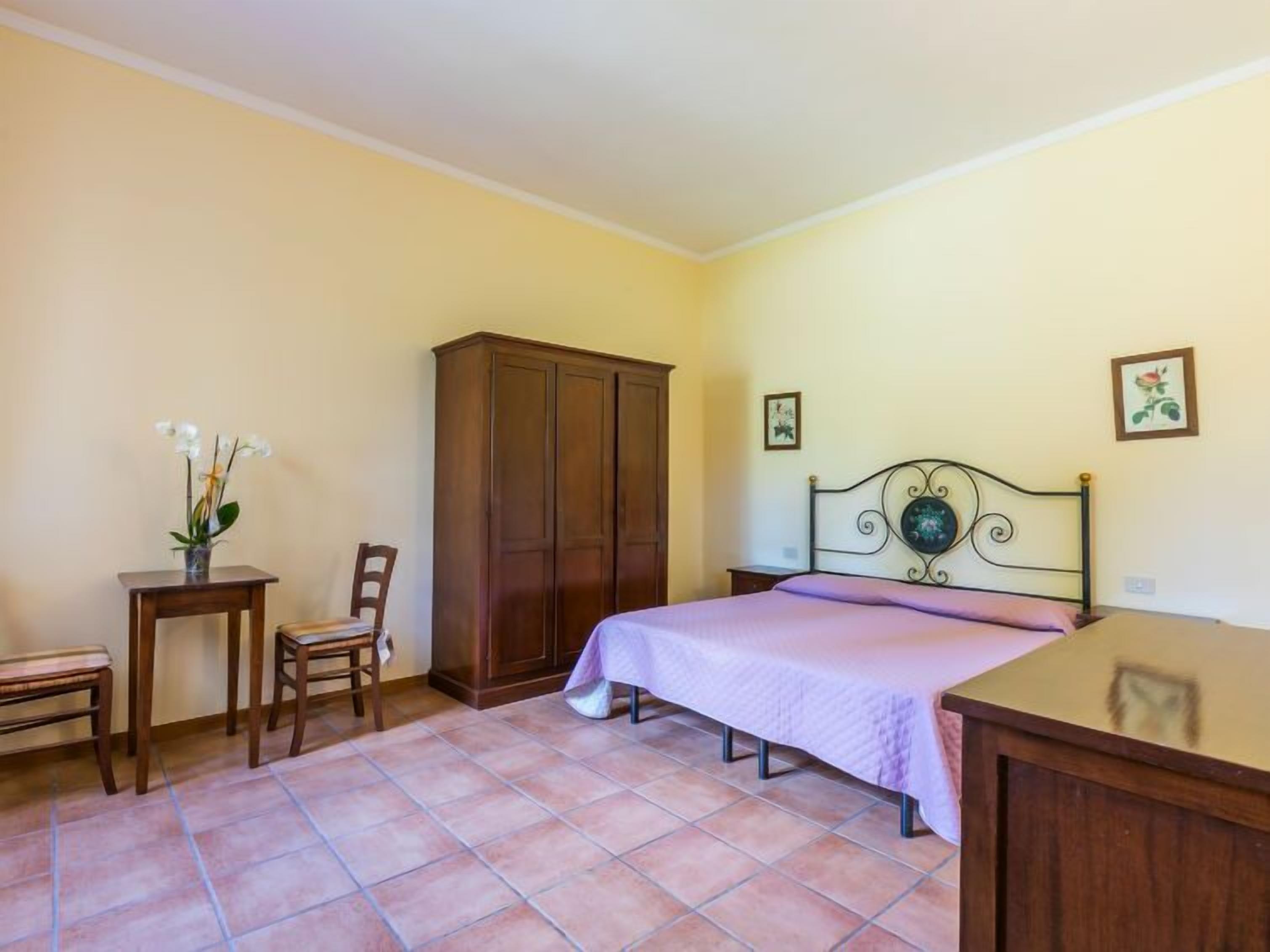 Quarto com cama, guarda-roupa, cadeira, mesinha e um vaso com flores.