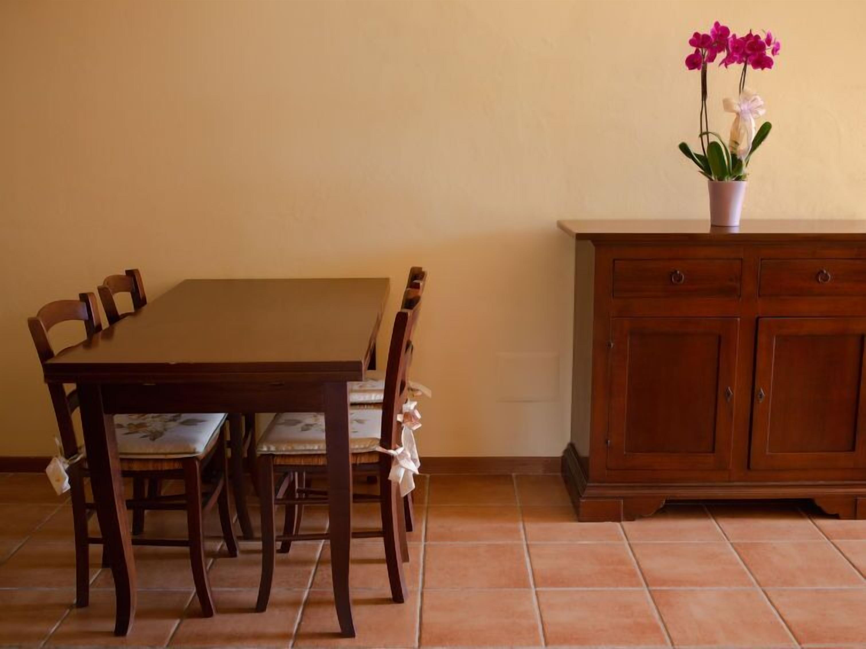 A dining area with a wooden table and chairs, a cabinet, and a potted plant with flowers.