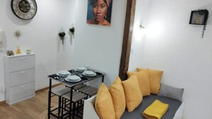 Un espace de vie compact comprenant un coin repas, un canapé avec des coussins jaunes et une petite table préparée pour le repas.