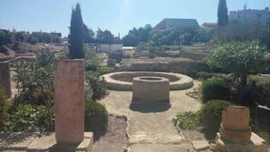 Une cour extérieure dotée d’une structure circulaire en pierre, entourée de verdure et bordée de bâtiments en arrière-plan.