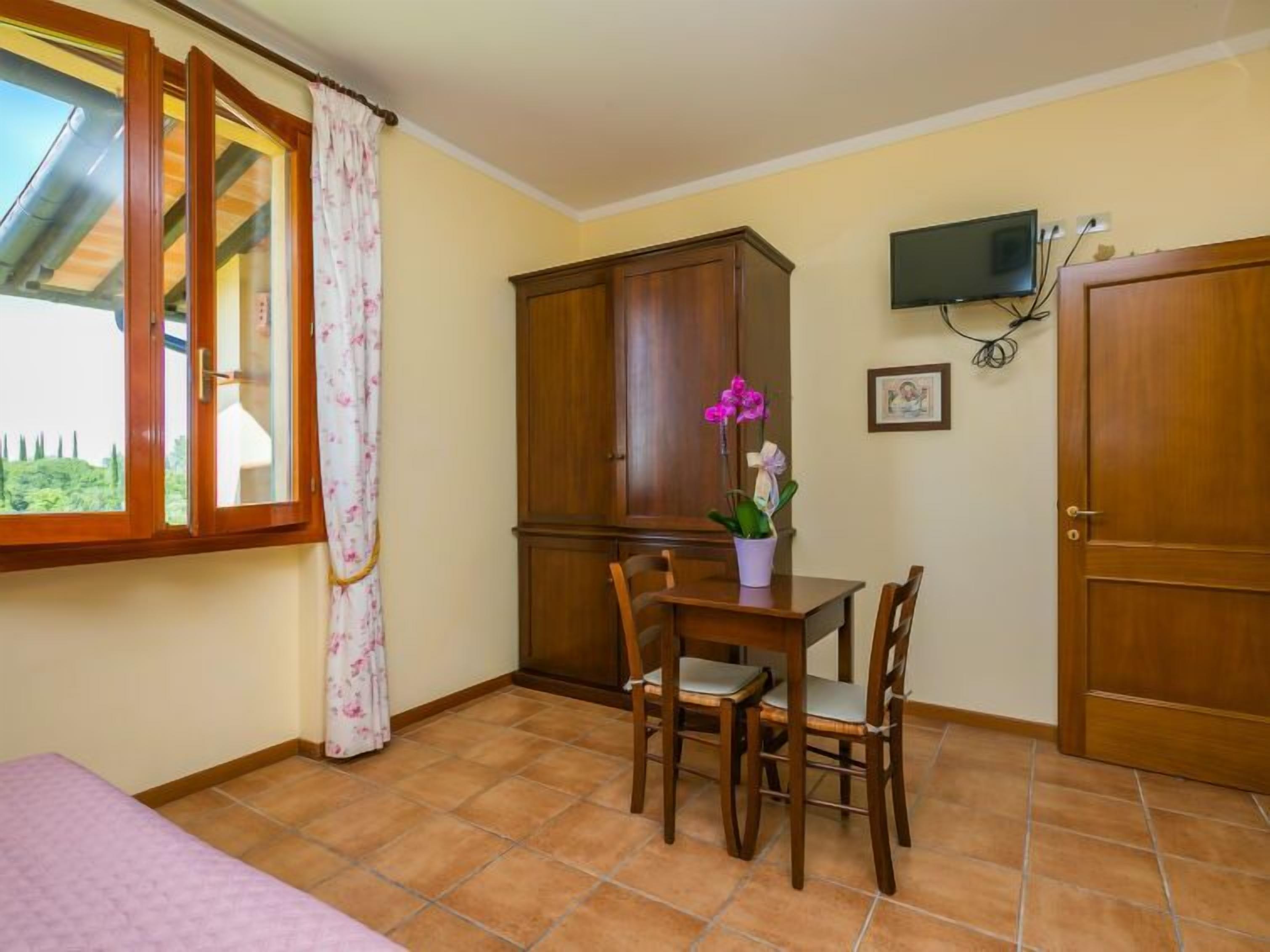 Ein Zimmer mit einem Bett, einem Holzkasten, einem Esstisch mit Stühlen, einer Orchidee im Blumentopf und einem Fernseher an der Wand.