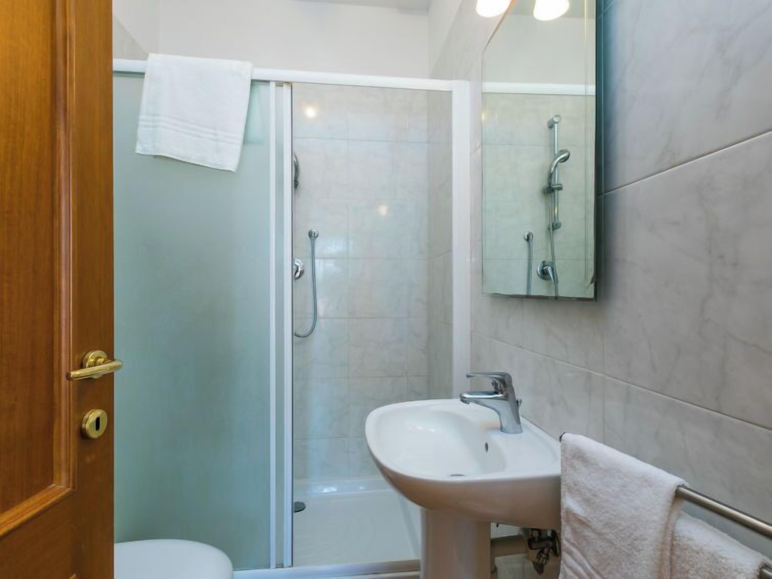 Un baño con cabina de ducha de vidrio, un lavamanos blanco y un espejo.
