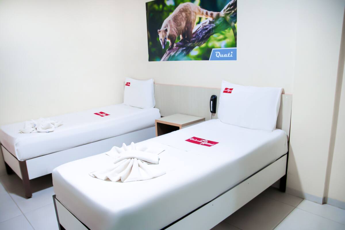 Two single beds with white linens and red pillows, a small bedside table, and a wall-mounted phone.