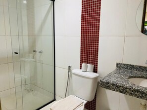 Ein Badezimmer mit einer gläsernen Duschkabine, einer Toilette mit rotem Fliesenbelag an der Wand und einem Waschbecken mit Granitplatte.
