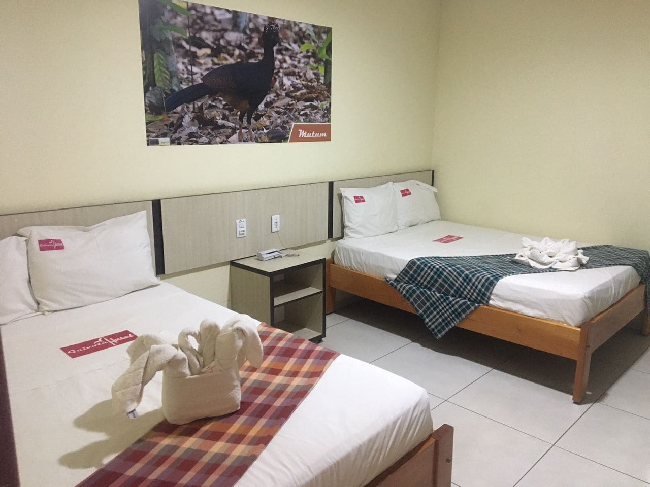 A hotel room with two beds, a small table, and a wall-mounted picture.