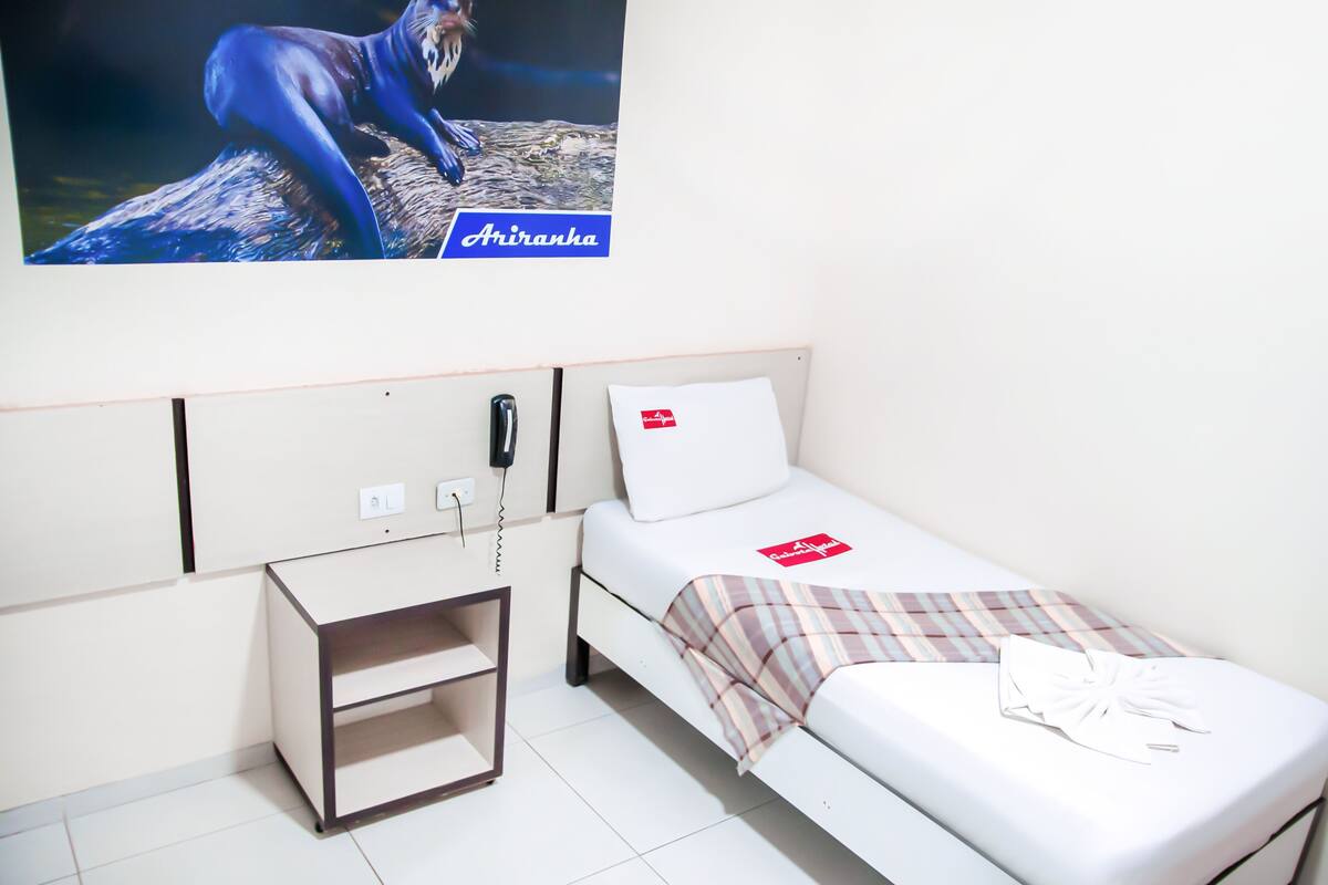 A hotel room with a bed, a bedside table, a phone, and a wall-mounted artwork.
