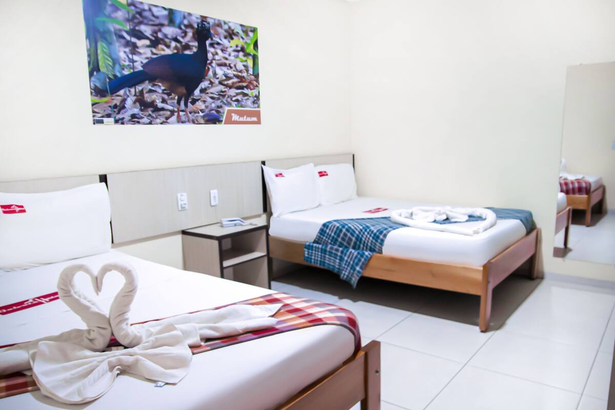 A hotel room with two beds, a nightstand, a wall-mounted TV, and a mirror.