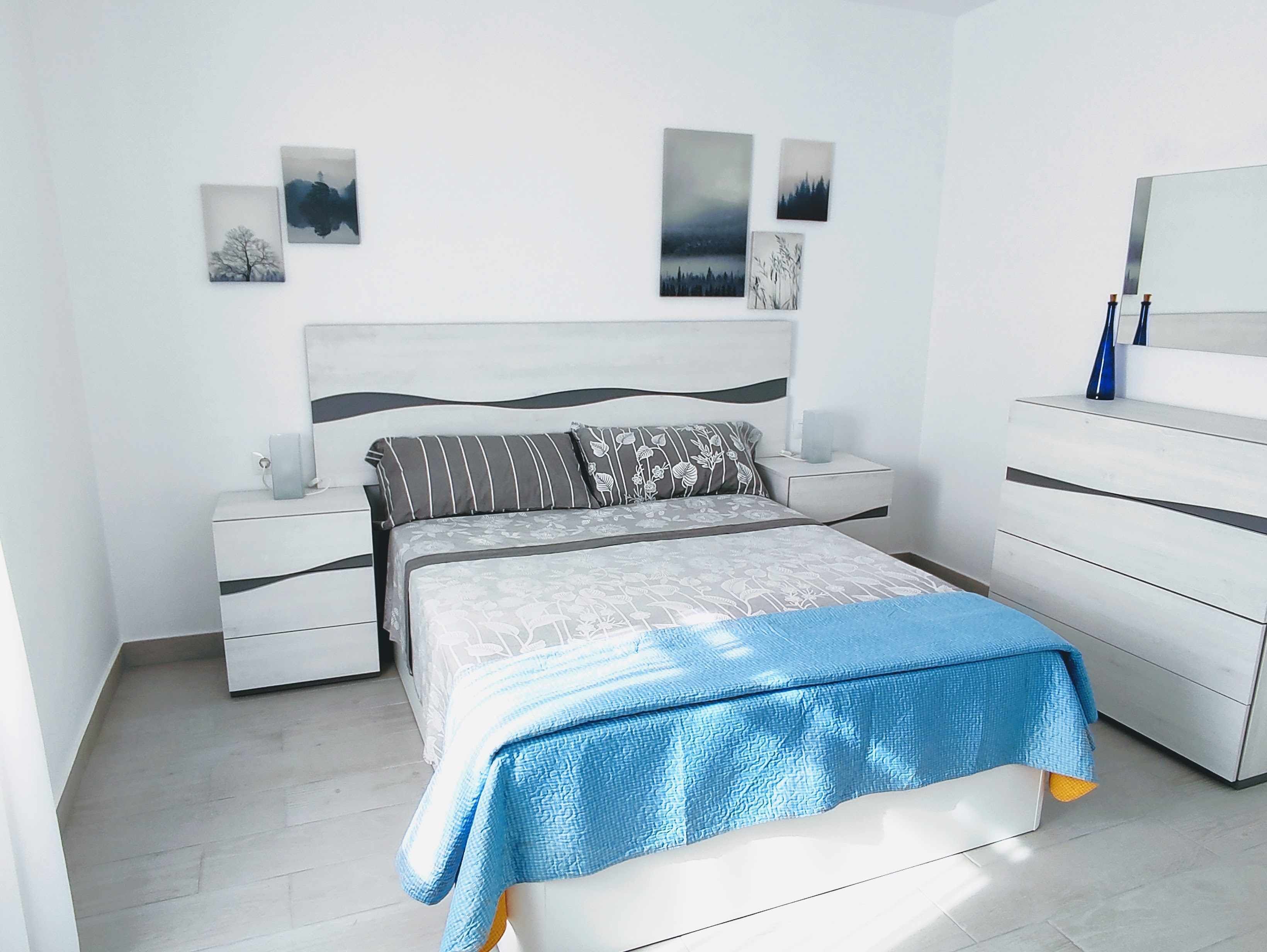 Ein modernes Schlafzimmer mit einem Bett, Nachttischen, einer Kommode und Wandbildern.