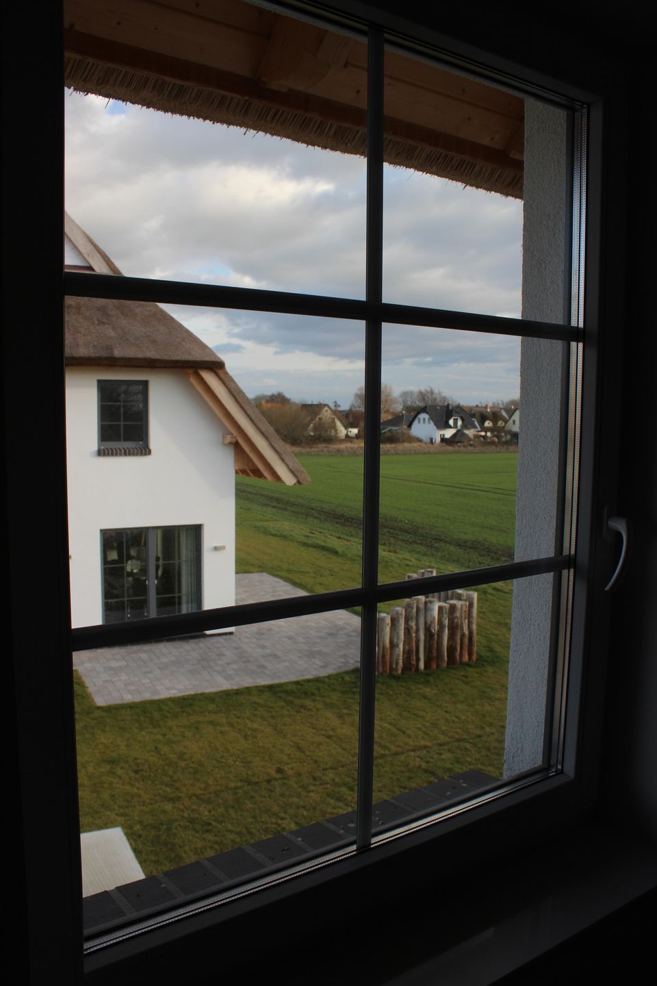 A window with a view of a house and a grassy field.