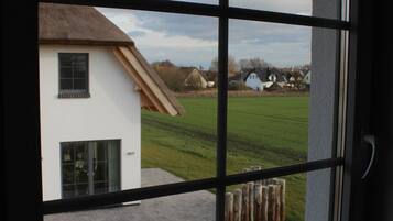A window with a view of a house and a grassy field.