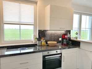 Eine Küche mit Einbauofen, Kaffeemaschine und einem Fenster mit Blick auf ein grünes Feld.