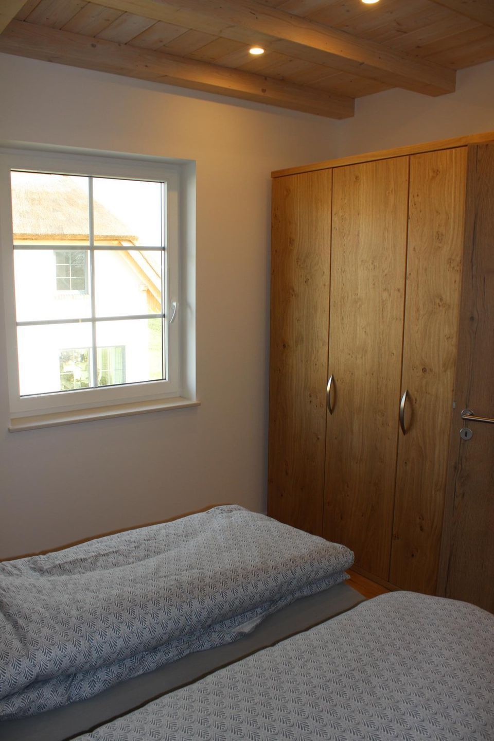 A bedroom with a wooden wardrobe, a window, and a bed with patterned bedding.
