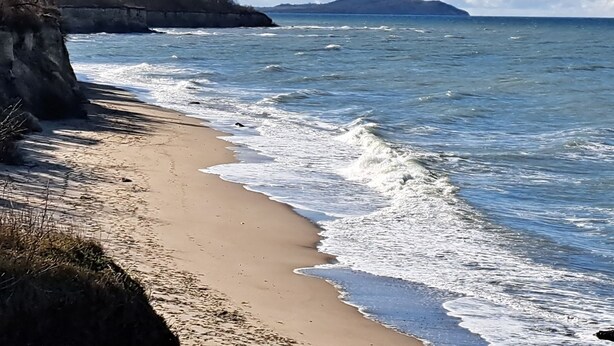 A beach with clear skies, a sandy shore, and a distant island.