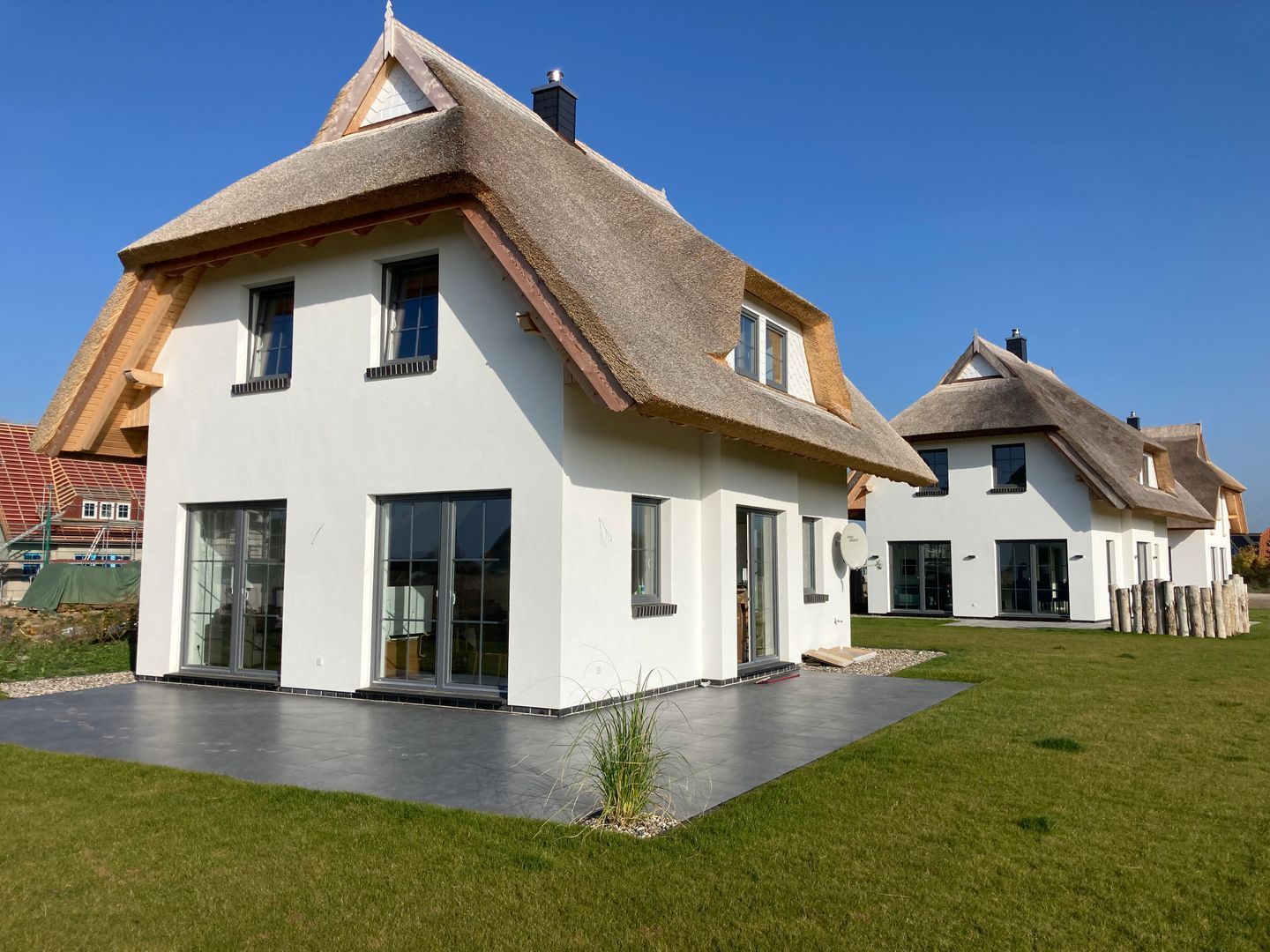 A modern house with a white exterior, large windows, and a thatched roof.