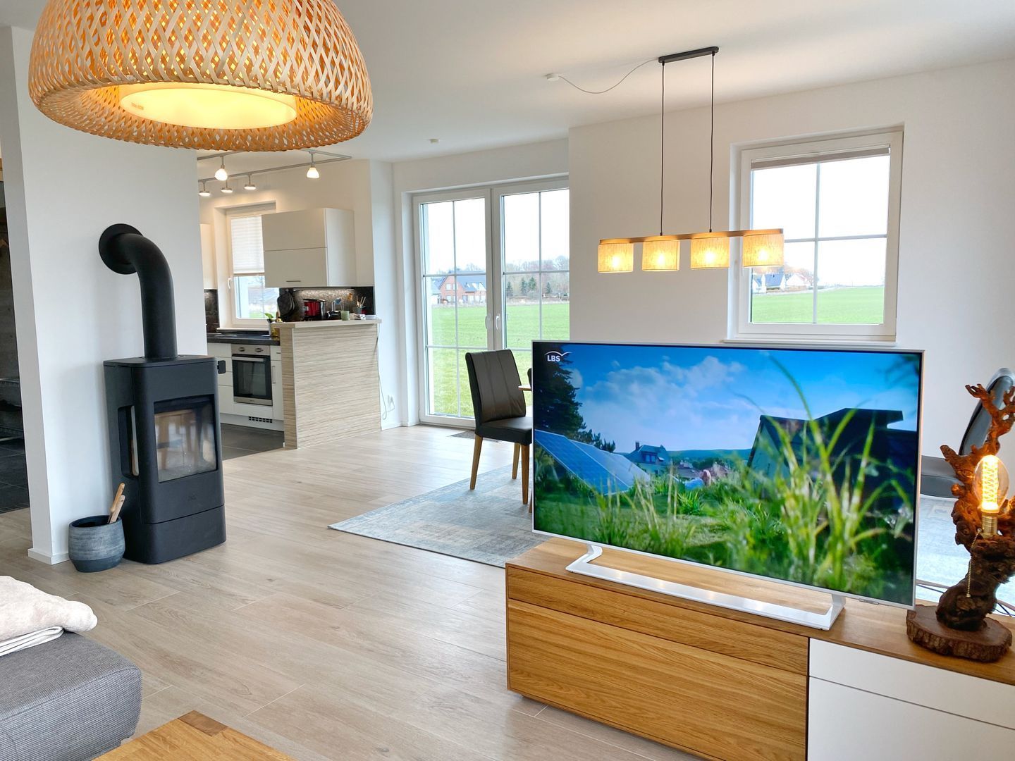 A modern living room with a large flat-screen TV, a fireplace, and a kitchen in the background.
