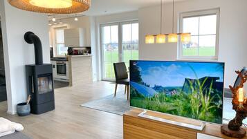 A modern living room with a large flat-screen TV, a fireplace, and a kitchen in the background.