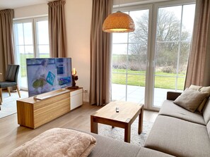 A modern living room with a television, sofa, coffee table, and a view of a garden through large windows.