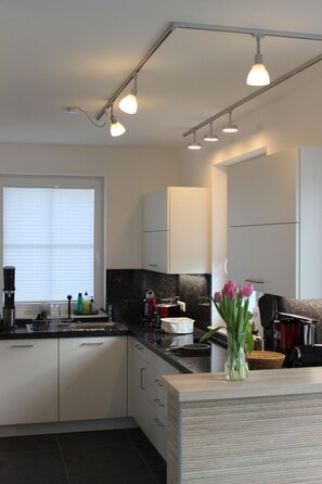 A modern kitchen with white cabinets, a black countertop, and a window with blinds. - Vacation home "Distelfink" in Dranske / Lancken - thatched roof house with Bodden view, (Dranske)