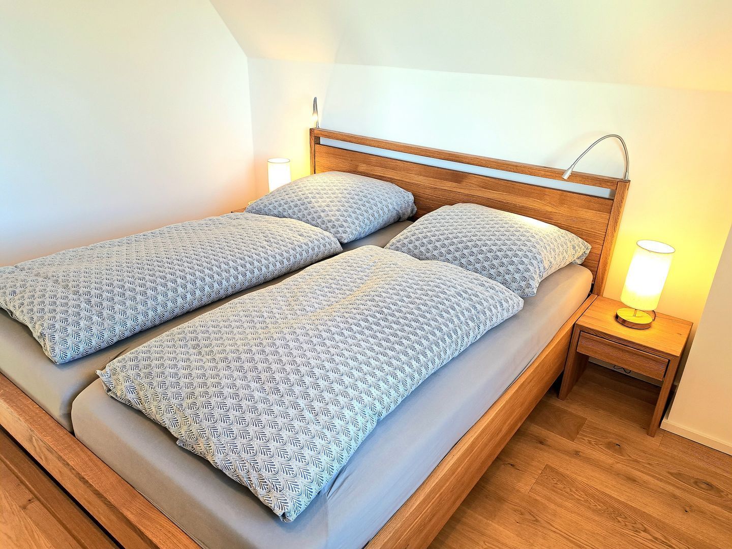Un lit double avec une literie à motifs, une tête de lit en bois, une table de chevet avec une lampe et un plancher en bois.