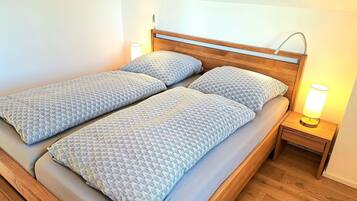 Un lit double avec une literie à motifs, une tête de lit en bois, une table de chevet avec une lampe et un plancher en bois.