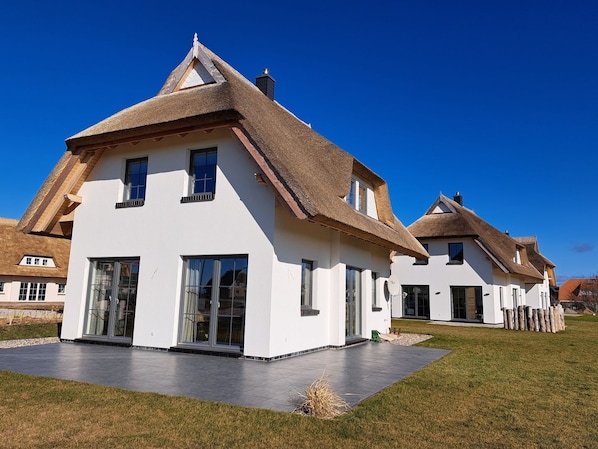 A modern house with a white exterior, large windows, and a thatched roof.